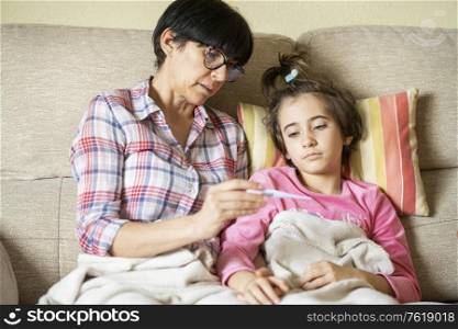 Mother measuring her daughter&rsquo;s temperature with a digital thermometer to check for fever. Mother measuring her daughter&rsquo;s temperature to check for fever