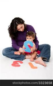 Mother, nanny, or teacher teaching baby to learn how to count one, two, three, with numbers in a playful way, while sitting on floor.