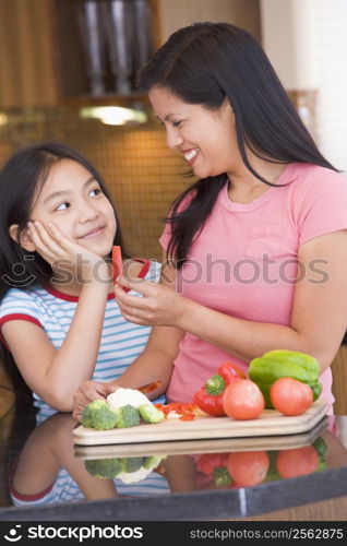 Mother Offering Daughter A Piece Of Freshly Chopped Pepper