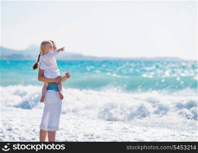 Mother on sea shore with baby pointing on copy space