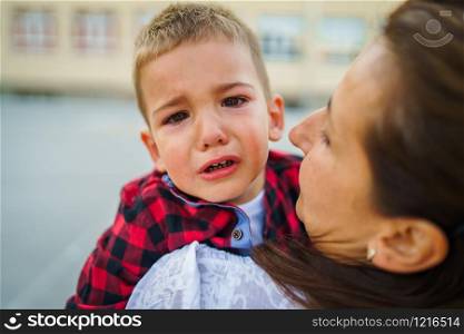 Mother or grandmother is holding small little boy child son crying in summer day outdoor