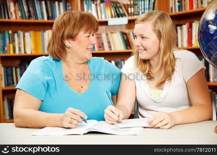 Mother or teacher helping a teenage girl study in the school library.