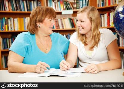 Mother or teacher helping a teenage girl study in the school library.