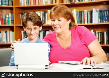 Mother (or teacher) helps her young son study on a computer in the library.