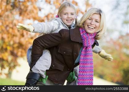Mother outdoors piggybacking daughter and smiling (selective focus)