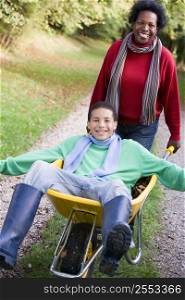 Mother outdoors pushing son in wheelbarrow and smiling (selective focus)