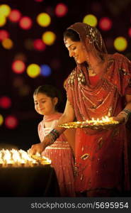 Mother placing diyas on a table while her daughter looks on