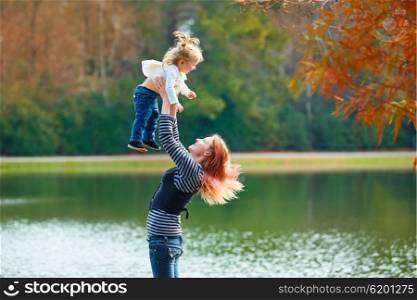 Mother playing throwing up baby girl daughter in the park lake
