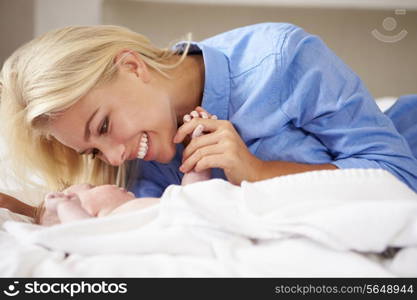 Mother Playing With Baby Girl As They Lie In Bed Together