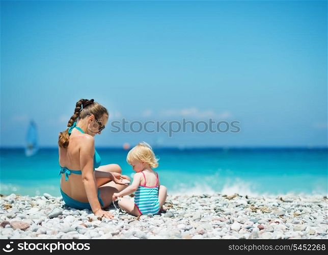 Mother playing with baby on beach. Rear view