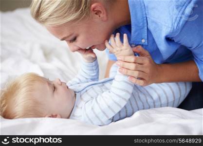 Mother Playing With Baby Son As They Lie In Bed Together