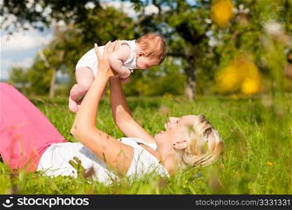 Mother playing with her baby on a great sunny day in a meadow with lots of green grass and wild flowers
