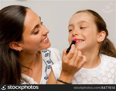 Mother playing with her daughter applying lipstick