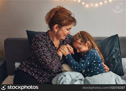 Mother playing with her little daughter in bed, having fun before going sleep. Mom tickling her cute daughter before bedtime