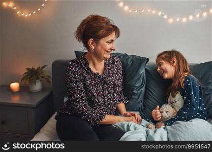 Mother playing with her little daughter in bed, having fun before going sleep. Mom telling her cute daughter funny stories before bedtime