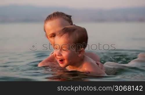 Mother playing with her young son in the beach waters during sunset