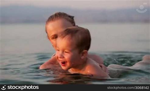 Mother playing with her young son in the beach waters during sunset