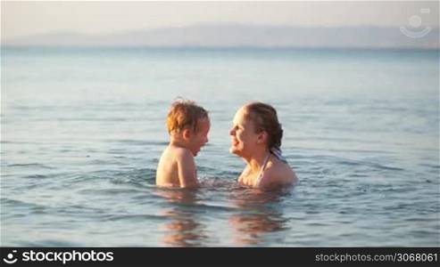 Mother playing with her young son in the sea holding him above water and kissing him on the cheek as they enjoy a tranquil summer day on their vacation, with copyspace