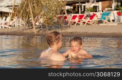 Mother playing with her young son tossing him up in the beach waters in a sunny day during holidays