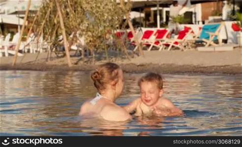 Mother playing with her young son tossing him up in the beach waters in a sunny day during holidays