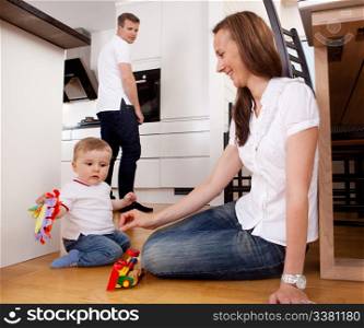 Mother playing with son on kitchen floor with father in background