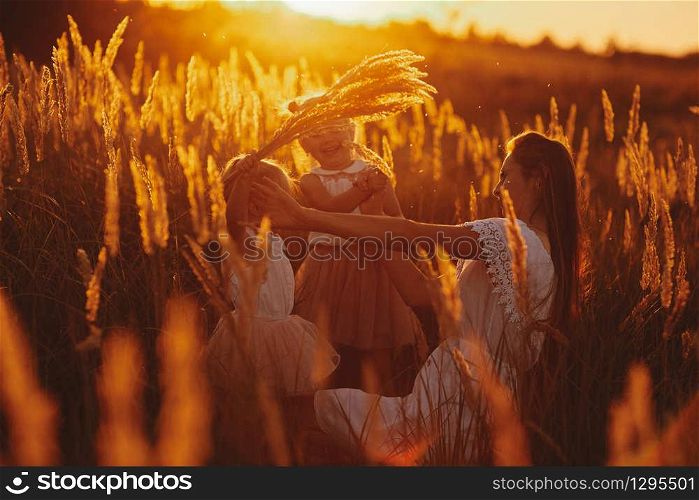 Mother plays with her daughter on the street in the park at sunset. happy family, mom and two daughters.. happy family, mom and two daughters. Mother plays with her daughter on the street in the park at sunset.