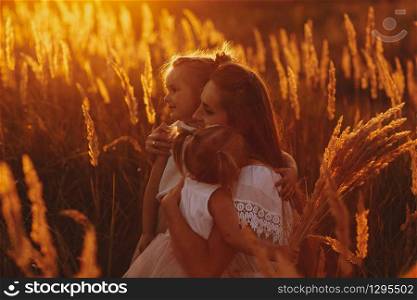 Mother plays with her daughter on the street in the park at sunset. happy family, mom and two daughters.. happy family, mom and two daughters. Mother plays with her daughter on the street in the park at sunset.