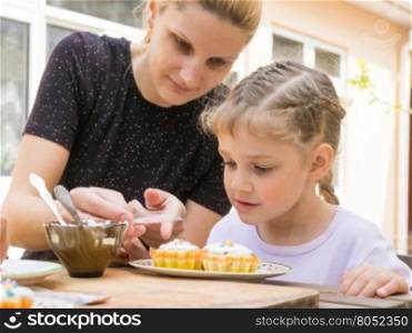 Mother pours a bag of confectionery posypku on Easter cupcake, daughter happily looking