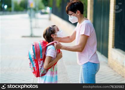 Mother preparing her little girl for the return to school wearing a mask. Back to school concept.. Mother preparing her little girl for the return to school wearing a mask.