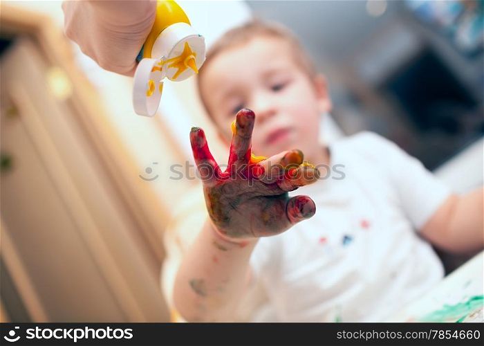 Mother pressing yellow finger-paint on colored boys hand