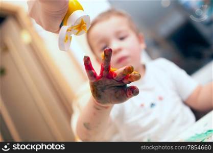 Mother pressing yellow finger-paint on colored boys hand