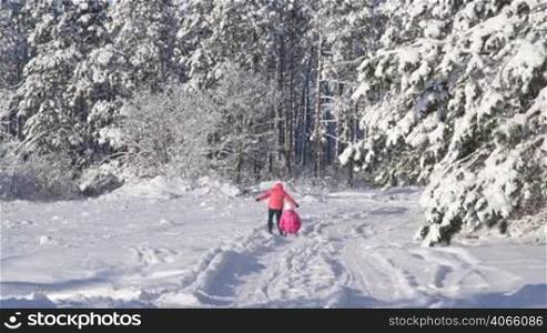 Mother pulling child on sled through snow in winter forest