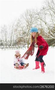 Mother Pulling Daughter On Sledge Through Snowy Landscape