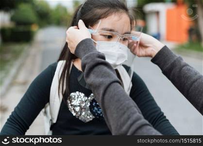 Mother puts a safety mask on daughter face for protection Covid-19 or coronavirus outbreak in village park to prepare go to school. Back to school concept. Medical mask to prevent coronavirus.