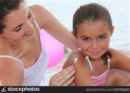 Mother putting suncream on her daughter.