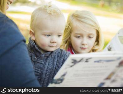 Mother Reading a Book to Her Two Adorable Blonde Children Wearing Winter Coats Outdoors.