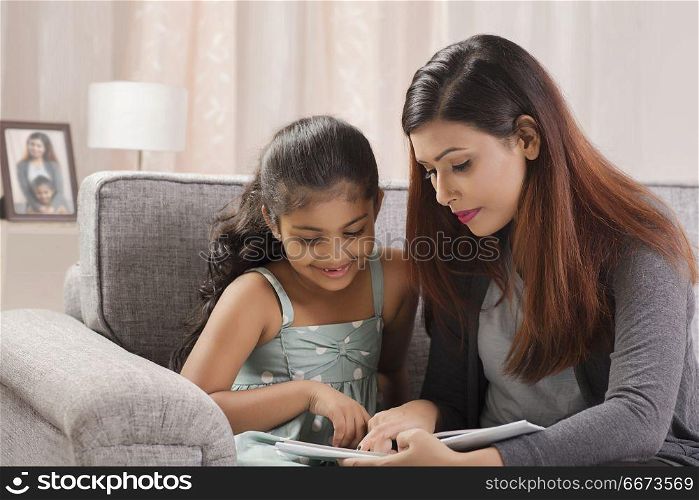 Mother reading book to daughter while sitting on sofa at home