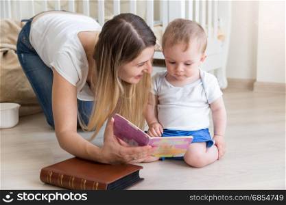 Mother reading book to her 10 months old baby boy on floor at living room