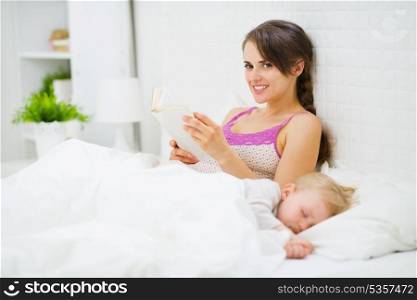 Mother reading in bed while baby sleeping|free time, self time