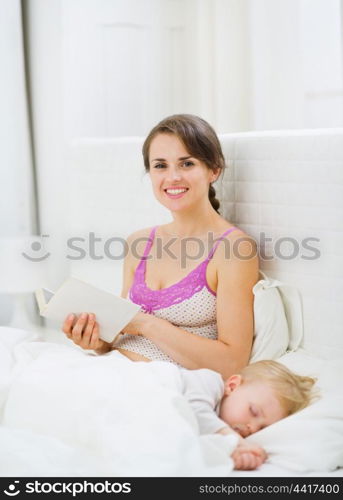 Mother reading in bed while kid sleeping