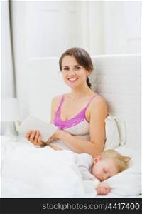 Mother reading in bed while kid sleeping
