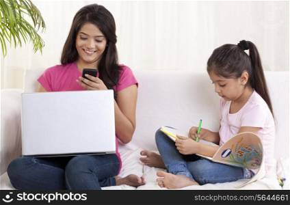 Mother reading text message on phone with daughter sitting besides her and drawing