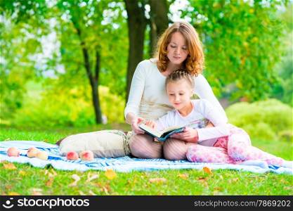 mother reads her daughter an interesting book in the park