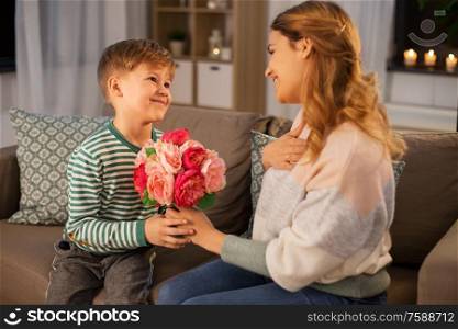 mother&rsquo;s day, holidays and family concept - happy little son giving flowers to his mother at home in evening. smiling little son gives flowers to mother at home
