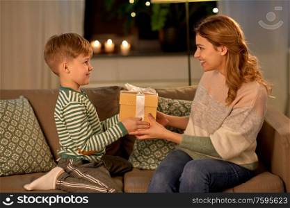 mother&rsquo;s day, holidays and family concept - happy little son giving present to his mother at home in evening. little son giving present to mother at home