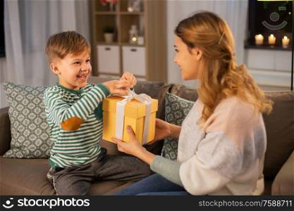 mother&rsquo;s day, holidays and family concept - smiling mother giving present to her happy little son at home in evening. mother giving present to her little son at home