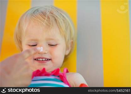 Mother&rsquo;s hand applying sun block creme on baby nose