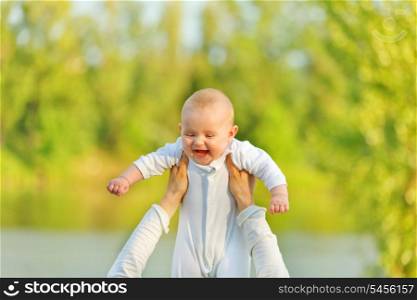 Mother&rsquo;s hands holding laughing baby girl against sunny leaves. Baby looking on mother.&#xA;