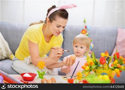 Mother showing baby how to paint on Easter egg