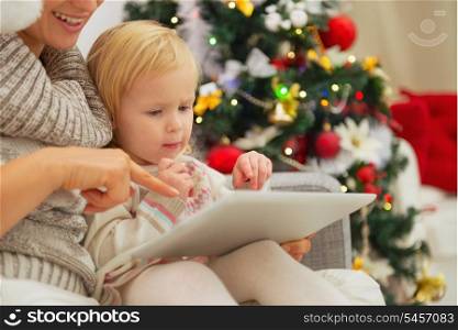 Mother showing baby something in tablet PC near Christmas tree